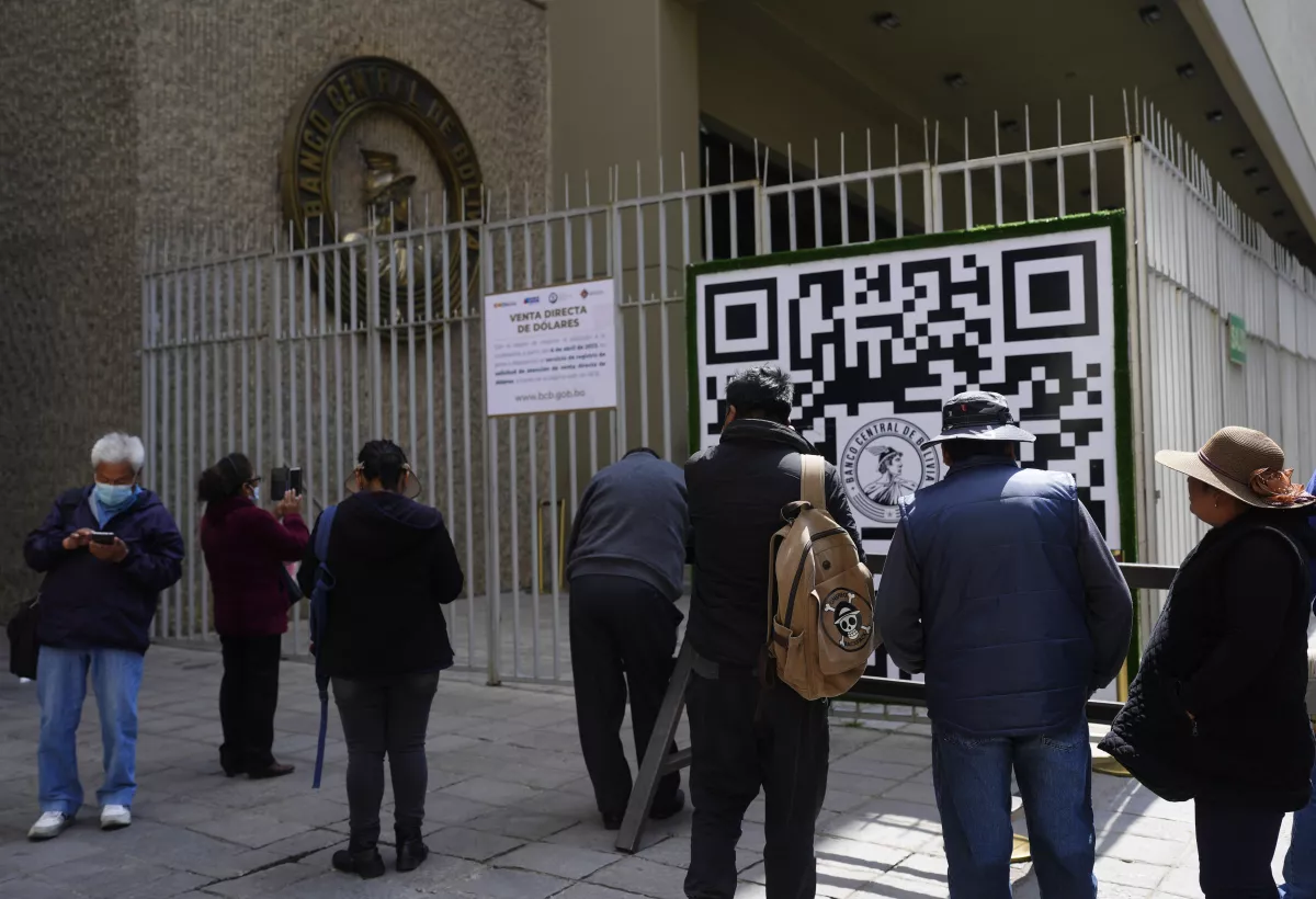 Varias personas miran un código QR afuera del Banco Central de Bolivia que las personas deben usar para registrarse a fin de hacer una cita con el banco que luego le dice al usuario cuántos dólares estadounidenses puede comprar en esa fecha, el martes 11 de abril de 2023 en La Paz, Bolivia.(Juan Karita / Associated Press)